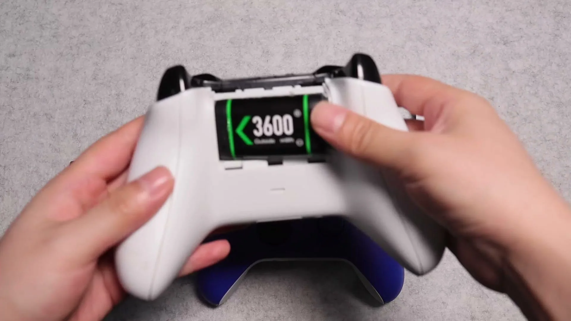 Two hands pressing a battery pack into the open battery compartment of a white Xbox controller