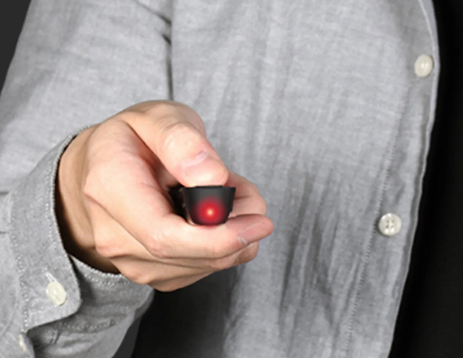 A hand holding a small presentation remote with a red light shining, a shirt in the background